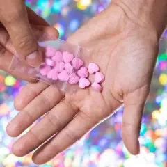 Różowe tabletki w kształcie serc w dłoni na tle kolorowych świateł.