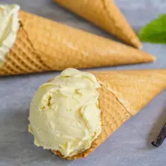 Drei Waffelkegel mit cremigem Vanilleeis, daneben eine Vanilleschote und ein Minzblatt.