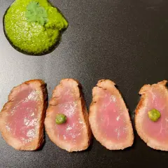 Cuatro lonchas de tataki de salmón con un toque de salsa verde y alcaparras, servidas en plato negro.
