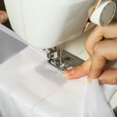 Dłonie szyją białą tkaninę na maszynie do szycia.