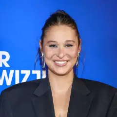 Uśmiechnięta Anna Szymańczyk w czarnej marynarce, z długimi kolczykami. Może właśnie wraca do męża po premierze?
