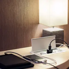 Elegancka ładowarka z gniazdkami i portami USB, idealna do tego, jak ukryć kable. Obok leżą tablet i smartfon.