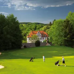 Zwei Golfer auf dem grünen Rasen des Golfclubs Schloss Georghausen, im Hintergrund das malerische Schloss.