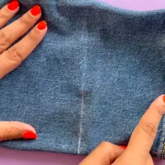 Main d'une femme avec un ongle rouge vif et une bague dorée, ajustant l'ourlet d'un jean.