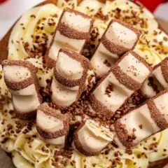 Tarta decorada con crema amarilla y trozos de tarta kinder bueno, espolvoreada con virutas de chocolate.
