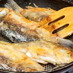 Smażone ryby na patelni z drewnianą łopatką.