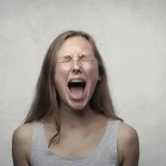 Ragazza con apparecchio dentale urla, occhi chiusi e fronte corrugata, un'espressione di pura paura di perdere il controllo.