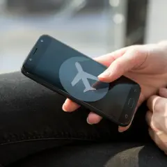Dłoń trzyma smartfon z ikoną samolotu. Zastanawiasz się, czy w trybie samolotowym działa budzik?