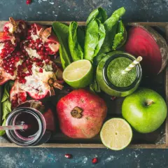 Frische Zutaten für eine **Detox Kur**: Granatapfel, grüner Saft, Rote Bete, Äpfel und Limetten in einer Holzkiste.