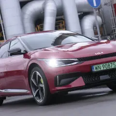 Czerwone Kia EV6 z zieloną tablicą rejestracyjną na tle przemysłowych rur.