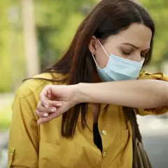 Mujer con mascarilla quirúrgica para que sirve, tose en el codo para evitar contagios.