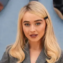 Mujer rubia con raya del pelo lateral, ojos azules y un clip negro en el cabello.