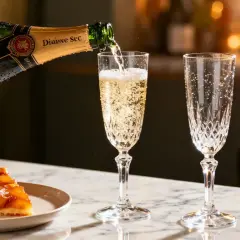 Une coupe de tarte aux fruits caramélisés est servie avec un verre de vin de dessert pétillant, versé d'une bouteille de champagne.