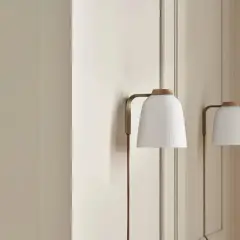 Elegancka lampa klinkiet z białym, plisowanym kloszem i drewnianą nakładką, subtelnie oświetla wnętrze.