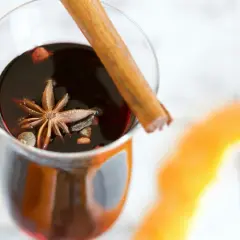 Un verre de vin chaud aux épices, parfait pour un marché de Noël. Une étoile de badiane et un bâton de cannelle flottent dans le liquide sombre.