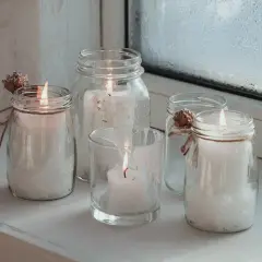 Fünf Windlichter mit Kerzen, die zum Windlicht selber machen inspirieren. Dekoriert mit Zapfen und Juteband.