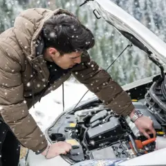 Un homme en doudoune vérifie le moteur de sa voiture sous la neige. Une astuce pour démarrage à froid diesel peut l'aider.