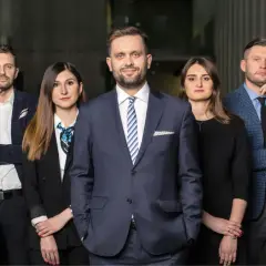 Grupa prawników w eleganckich strojach stoi przed nowoczesnym budynkiem.