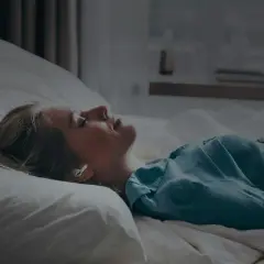 Kvinna med hörlurar i sängen, lyssnar på guidad meditation för avkoppling.