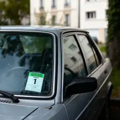 Autocollant de contrôle technique périmé 1 mois sur le pare-brise d'une voiture grise.
