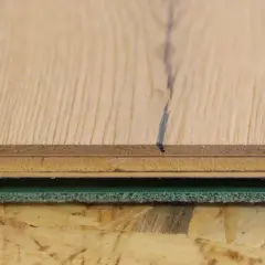 Detailaufnahme von Holzschichten und grüner Trittschalldämmung, bereit für das Parkett verlegen.