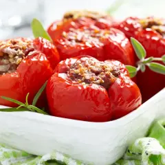 Peperoni ripieni di carne, cotti al forno e guarniti con erbe aromatiche, serviti in una ciotola bianca.
