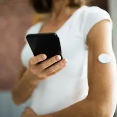 Kobieta z sensorem na ramieniu korzysta z aplikacji Libre 2 na telefonie, monitorując swoje zdrowie.