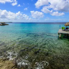 Bonaire wyspa: drewniany pomost z leżakami i parasolem, turkusowa woda, skaliste dno, chmury na niebie.