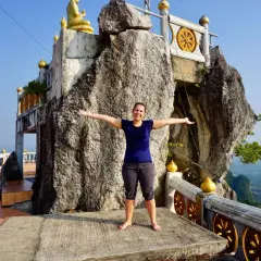 Frau steht vor einem Felsen, der wie ein Tigerhöhlentempel aussieht. Stufen führen zum Tempel.