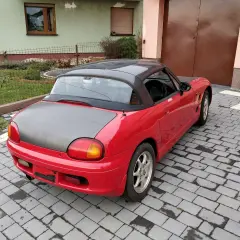 Czerwone Suzuki Cappuccino z czarnym dachem i maską stoi na podjeździe z kostki brukowej.
