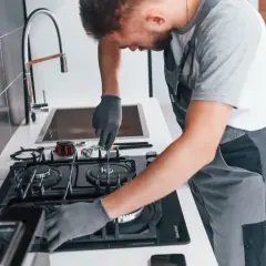 Fachowiec w rękawiczkach dokonuje podłączenia kuchenki gazowej. Narzędzia leżą obok.