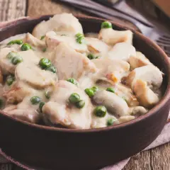 Pyszny strogonow z kurczaka z pieczarkami i groszkiem w kremowym sosie, podany w glinianej misce na drewnianym stole.