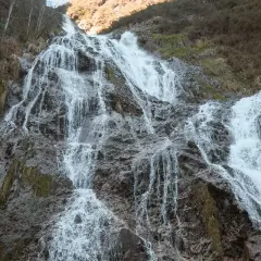 La cascada de Aitzondo desciende por una ladera rocosa, con agua blanca y espumosa que se abre paso entre la vegetación seca y las rocas grises.