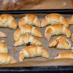 Szybkie rogaliki kruche, świeżo upieczone, leżą na blasze wyłożonej papierem do pieczenia. Niektóre z nich mają nadzienie.
