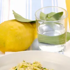 Un piatto di riso zucchine e limone, con un limone fresco e un bicchiere d'acqua.