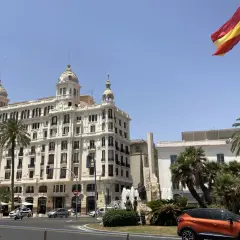 Alicante, pogoda marzec: słoneczny dzień, palmy i hiszpańska flaga nad białym budynkiem.
