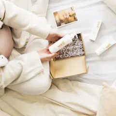Gravid kvinna öppnar ett paket med hudvårdsprodukter. En flaska med hyaluronsyra och en kräm för bristningar är synliga.