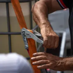 Dłonie mężczyzny obsługujące mechanizm napinający pomarańczową taśmę.