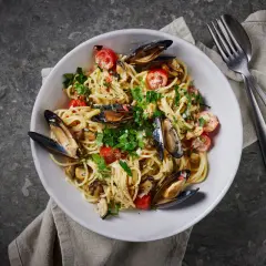 En skål med spaghetti vongole, toppad med färska örter och körsbärstomater. En klassisk italiensk rätt som passar perfekt för en mysig middag.