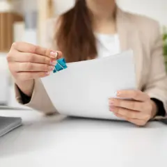 Kobieta z paznokciami ozdobionymi serduszkami trzyma dokumenty, przygotowując się do złożenia wypowiedzenia umowy najmu.