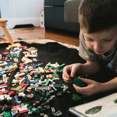 Chłopiec buduje z klocków LEGO, a obok leży instrukcja. Jak umyć klocki LEGO? Wystarczy je zebrać i umyć.