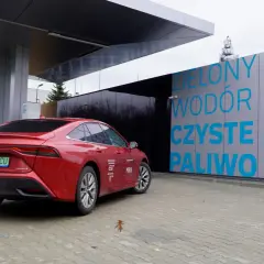 Czerwona Toyota Mirai na stacji tankowania wodoru. "Zielony wodór, czyste paliwo" - hasła na budynku stacji.