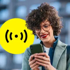 Kobieta z uśmiechem korzysta z telefonu, obok żółte koło z symbolem sygnału, sugerujące łatwe połączenie dzięki Revolut eSIM.