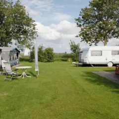 Słoneczny dzień na kempingu namiotowym. Dwa przyczepy kempingowe i namioty stoją na zielonej trawie, otoczone drzewami.