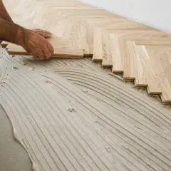Pose de parquet en chevrons. Des lames de bois clair sont posées sur un lit de colle ondulée.