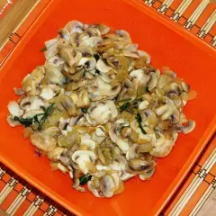 Champiñones salteados con cebolla y espinacas, servidos en un plato naranja sobre un mantel de bambú.