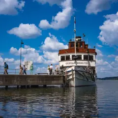 Folk väntar på en båt till Artipelag vid en brygga under en molnig men solig dag.