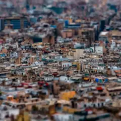 A dense cityscape rendered with tilt shift photography, making the buildings appear like miniature models.