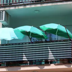 Trzy turkusowe parasole nad zasłoniętą balustradą na balkonie. Pomysł, jak zasłonić balustradę na balkonie, wykorzystując parasole.