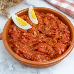 Un plato de asadillo manchego, con pimientos rojos guisados y adornado con gajos de huevo cocido.